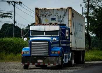 a blue semi truck driving down a rural road