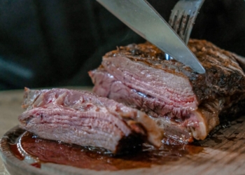 person slicing juicy medium rare meat on top of brown wooden cutting board