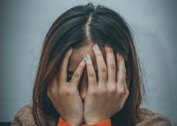 woman in brown sweater covering her face with her hand