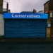 A blue closed shopfront with 'Conservatives' signage on a quiet urban street.
