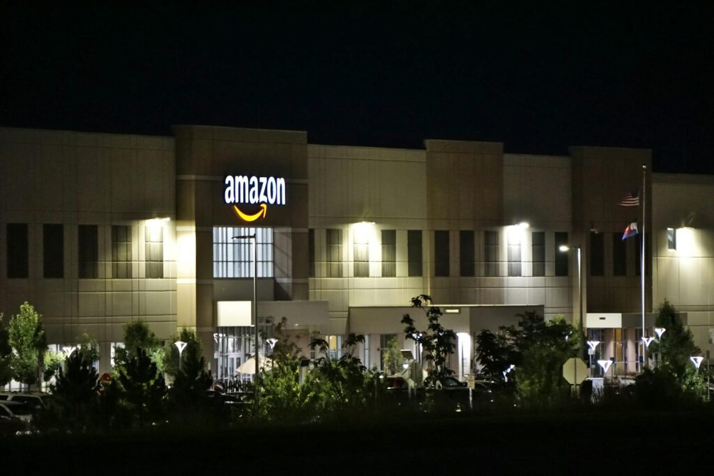 Amazon warehouse building illuminated at night with trees and signage.