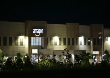 Amazon warehouse building illuminated at night with trees and signage.