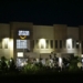 Amazon warehouse building illuminated at night with trees and signage.
