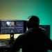 A video editor works on dual monitors with headphones, focusing on color correction.