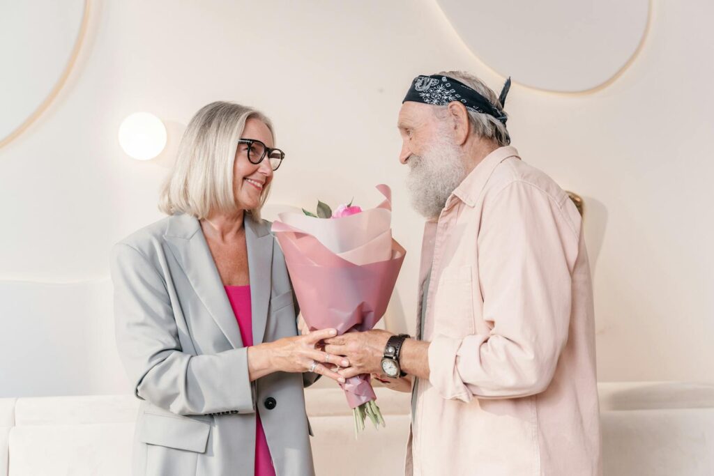 Charming moment of an elderly couple exchanging a bouquet indoors, showcasing love and togetherness.