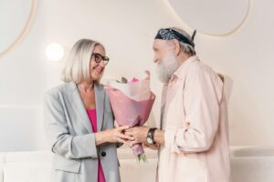 Charming moment of an elderly couple exchanging a bouquet indoors, showcasing love and togetherness.
