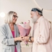 Charming moment of an elderly couple exchanging a bouquet indoors, showcasing love and togetherness.