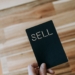 a person holding a black book with the word sell written on it