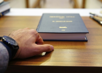 person holding black covered book on brown wooden table