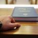 person holding black covered book on brown wooden table