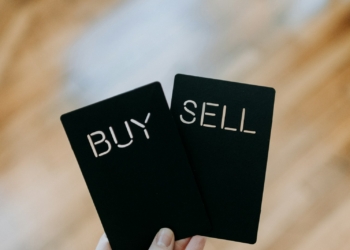 a hand holding two black cards with the words buy and sell written on them