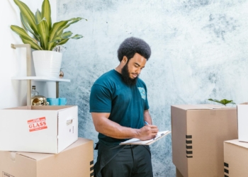A mover with a clipboard checking packages and boxes for relocation indoors.