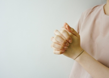 person wearing pink crew-neck shirt with hand clasped together