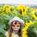 girl wearing red framed sunglasses and white hat surrounded by yellow sunflowers during daytime