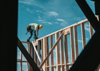 man in yellow shirt and blue denim jeans jumping on brown wooden railings under blue and