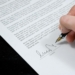 Close-up of a hand signing a formal document with a fountain pen, indicating agreement.