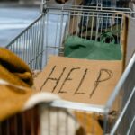 A shopping cart with a cardboard 'Help' sign and belongings, symbolizing urban homelessness.