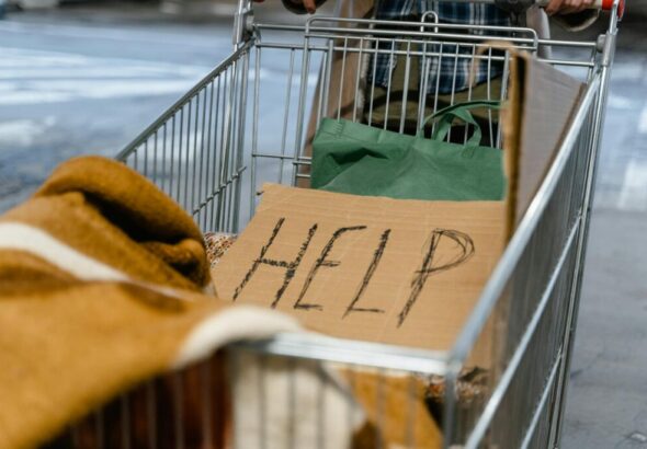 A shopping cart with a cardboard 'Help' sign and belongings, symbolizing urban homelessness.