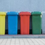four assorted-color trash bins beside gray wall