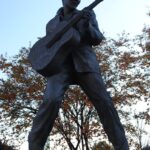 man holding stick statue under white sky during daytime