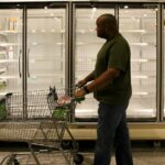 man in brown polo shirt and gray pants standing beside shopping cart