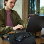 Young man uses laptop, portable storage device on table.
