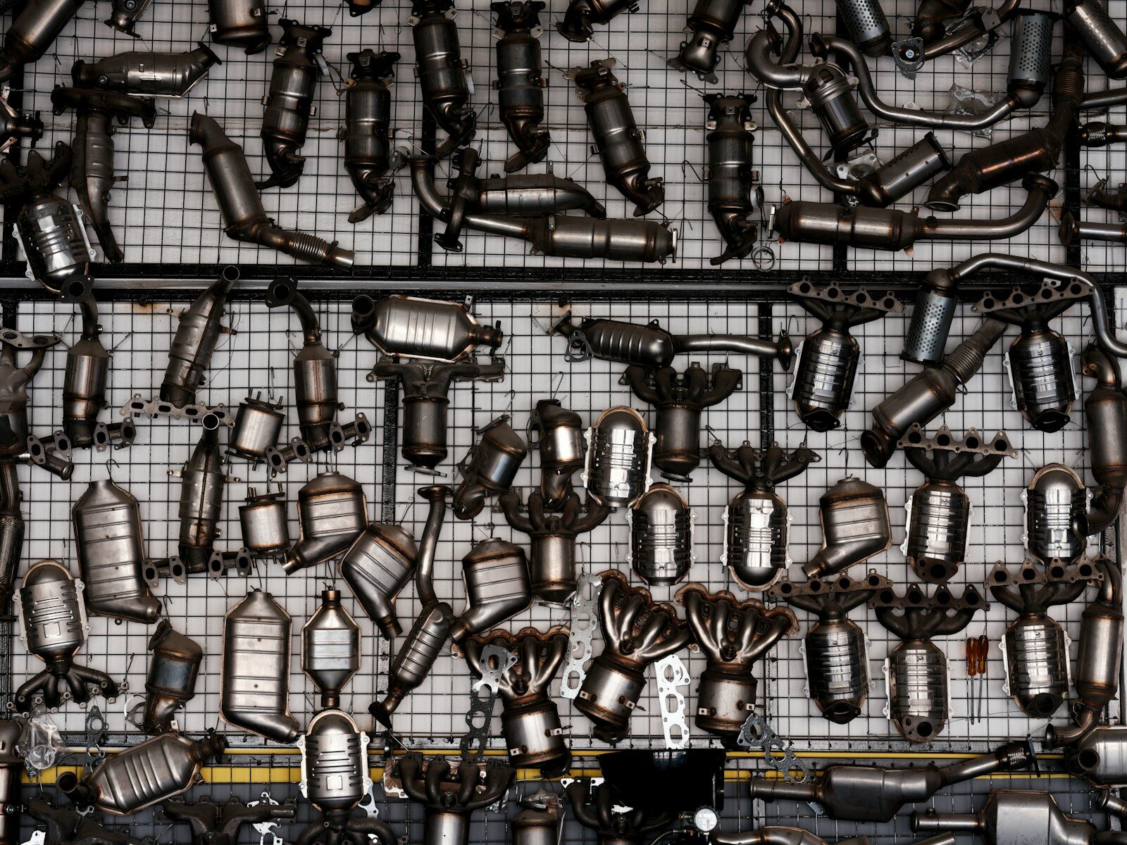 Many catalytic converters hanging on a grid wall.