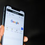 A hand holding a smartphone displaying the Google search engine homepage