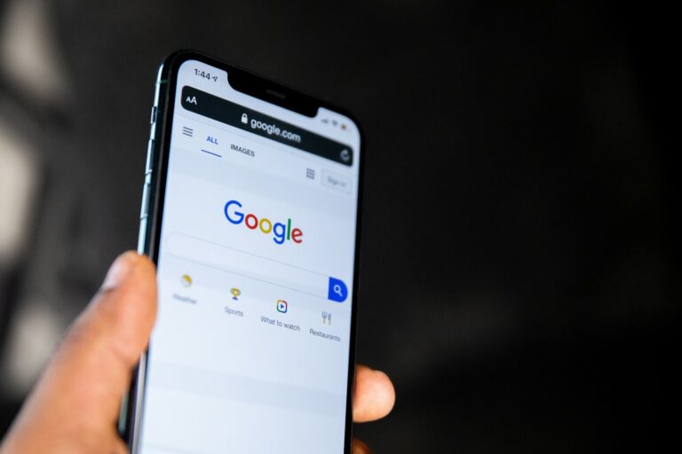 A hand holding a smartphone displaying the Google search engine homepage
