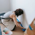 A woman applying adhesive tape to a wall for a renovation project indoors.