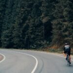 A cyclist riding a road bike on a winding asphalt road through a forest