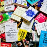 A large pile of various self-help and business books scattered on a surface