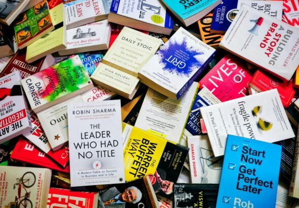 A large pile of various self-help and business books scattered on a surface