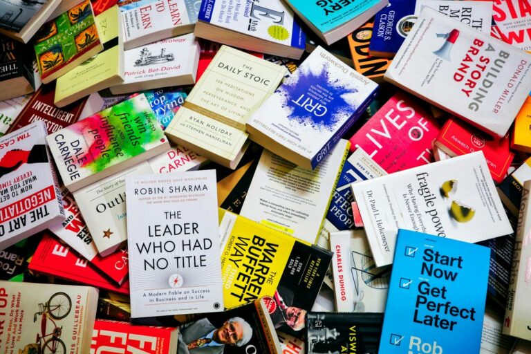 A large pile of various self-help and business books scattered on a surface