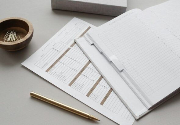 A finance tracker planner with budget sheets, a gold pen, and paper clips