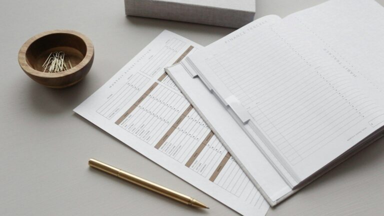 A finance tracker planner with budget sheets, a gold pen, and paper clips