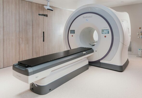 A white medical radiation therapy machine with a black patient table in a clinic