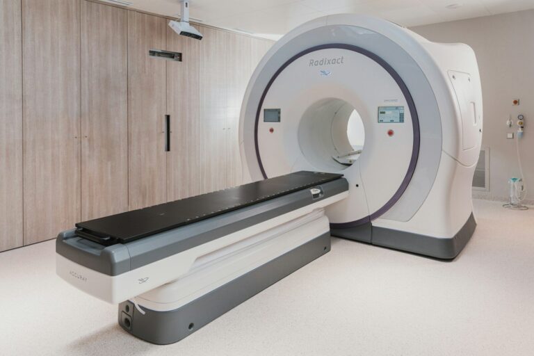 A white medical radiation therapy machine with a black patient table in a clinic