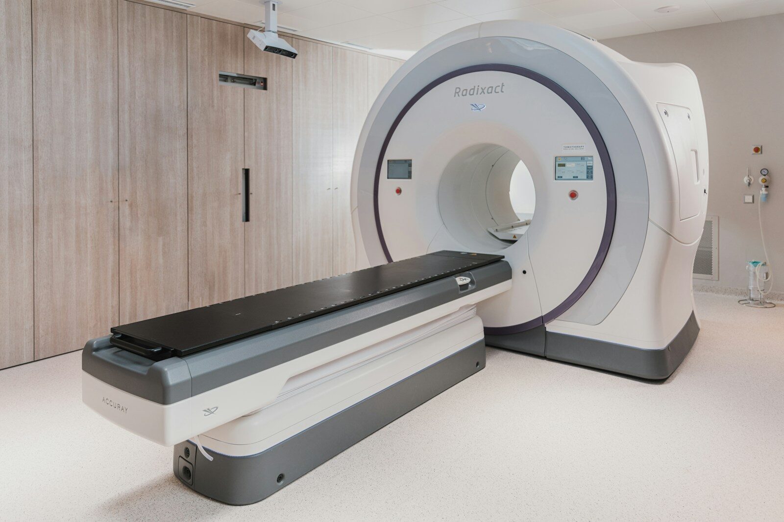 A white medical radiation therapy machine with a black patient table in a clinic