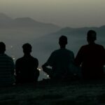 Five people sit on a hilltop overlooking a distant city