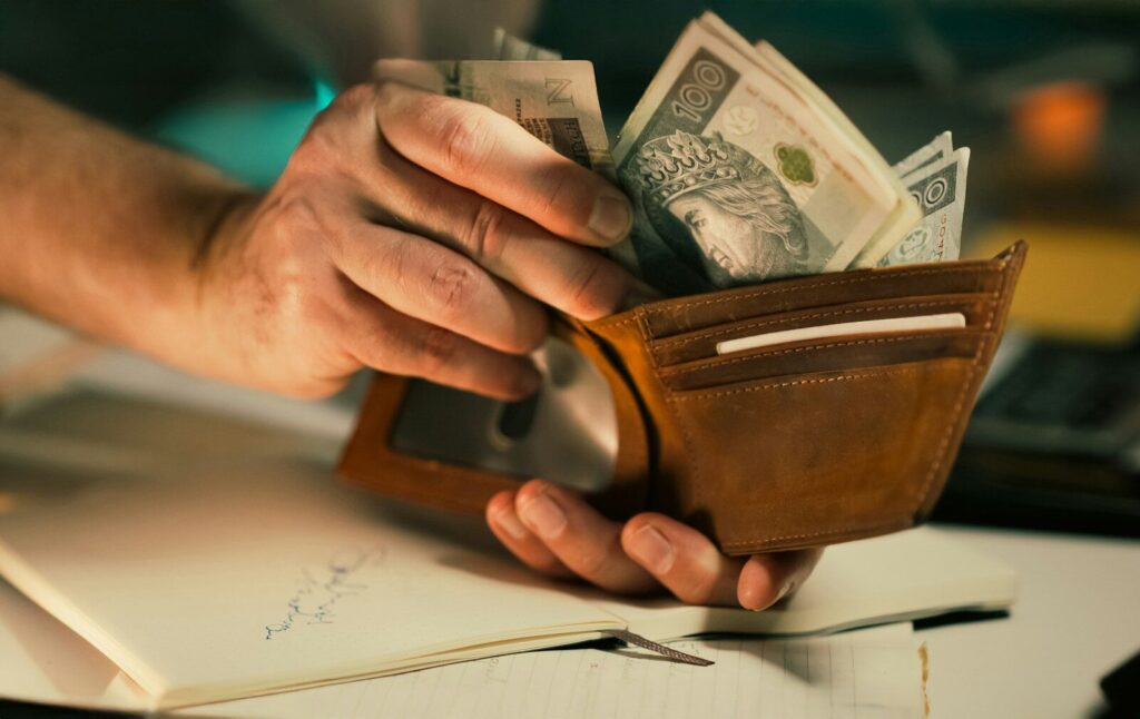 Hands holding us dollar bills in a brown leather wallet