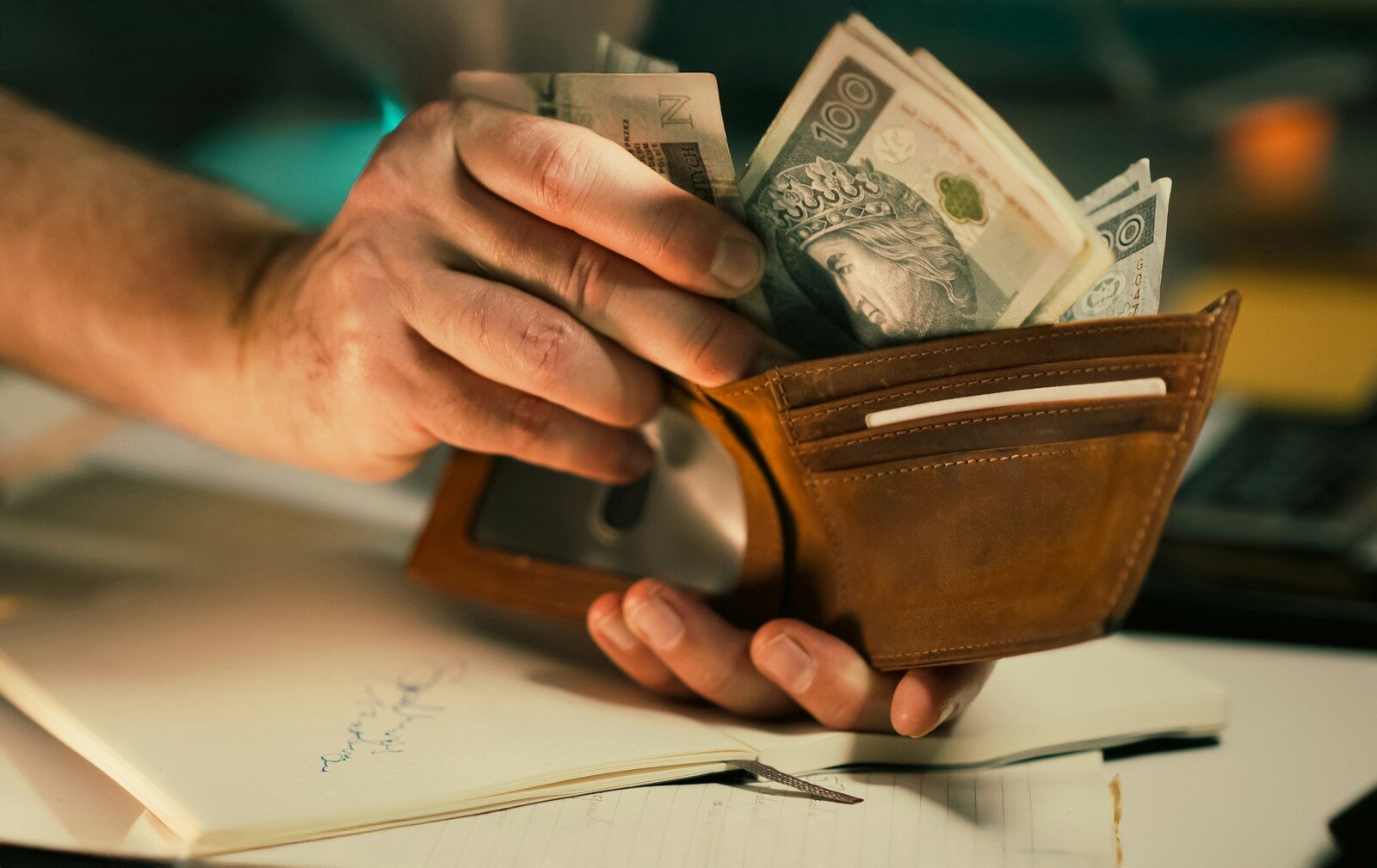 Hands holding us dollar bills in a brown leather wallet